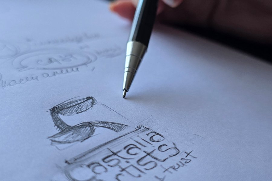 A hand sketching the Castalia logo on paper — a moment of creation capturing the birth of an idea and a community.