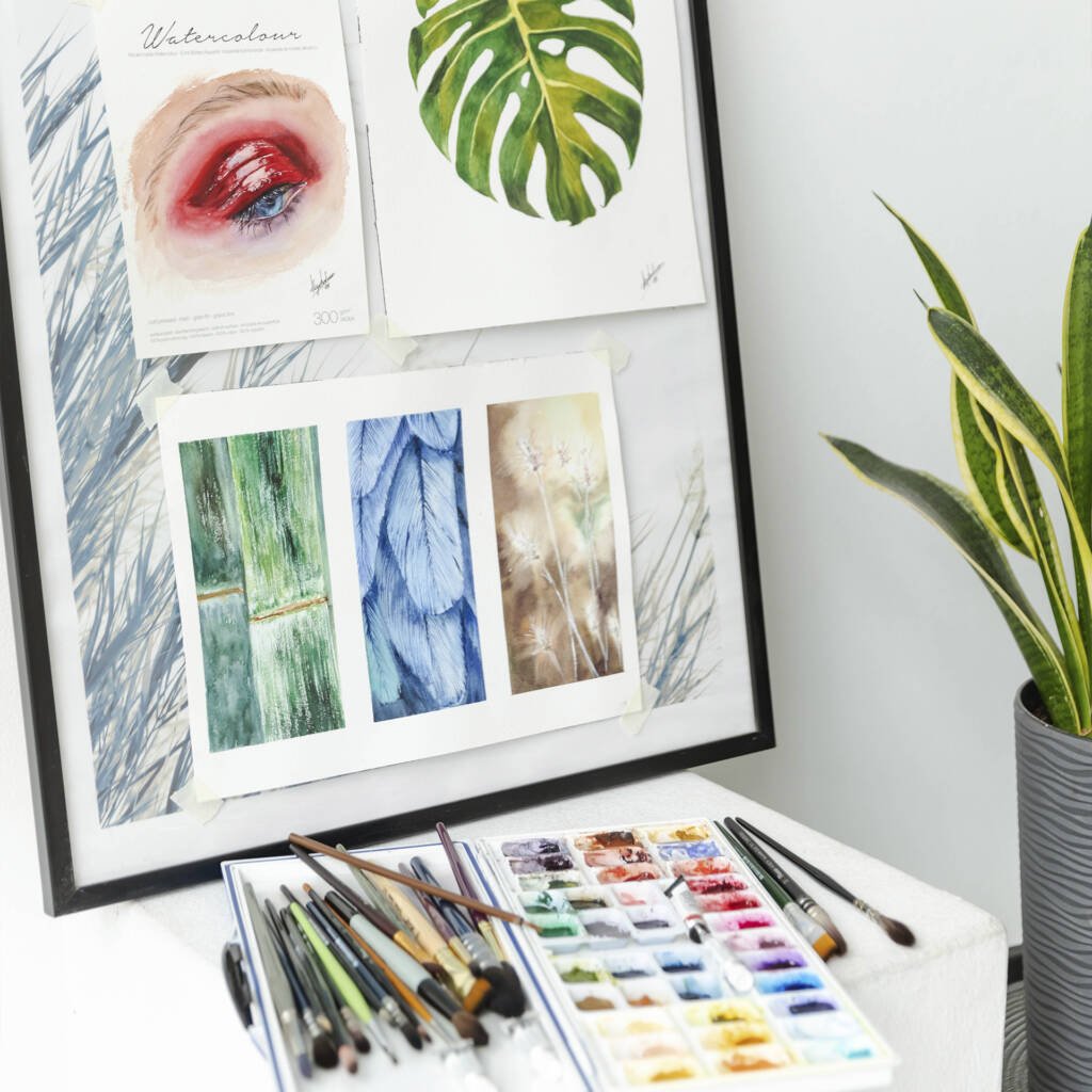 Close-up of Aliya Bodnar’s art studio featuring watercolor brushes, painting supplies, and framed artworks leaning on the wall in a bright, minimal interior.