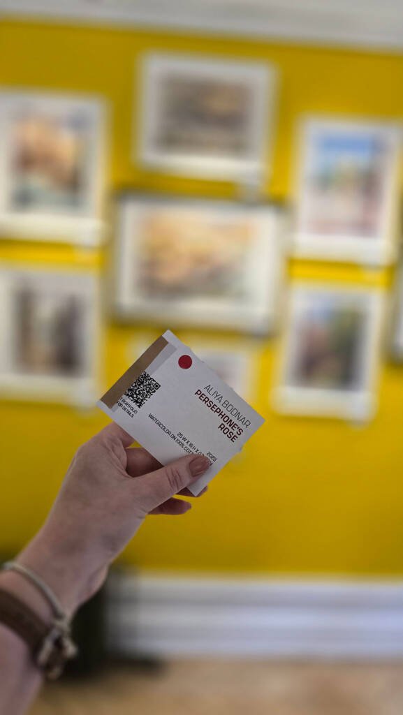 Aliya Bodnar holding the red dot sticker to mark her first painting sold at the solo exhibition.
