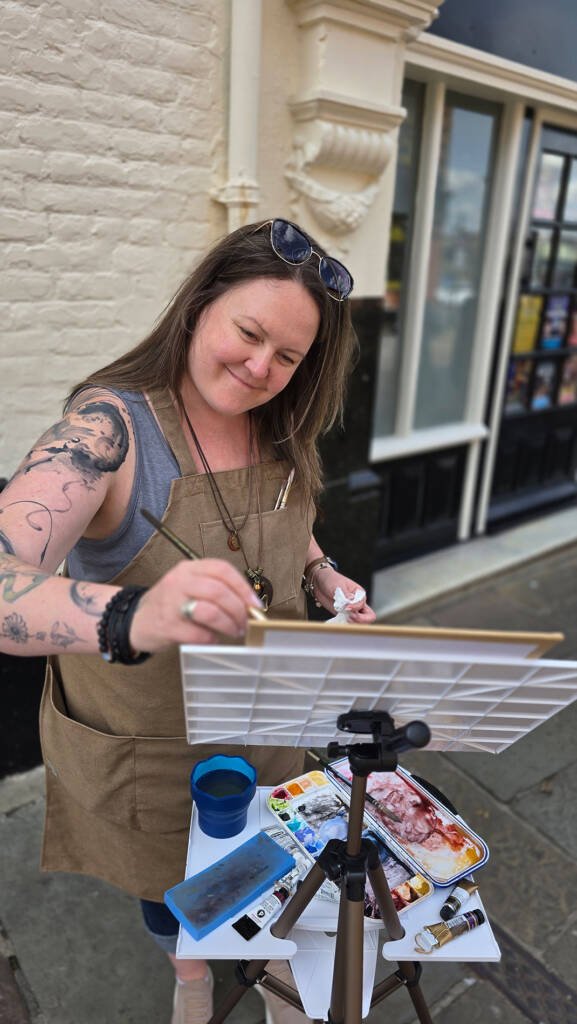 Aliya Bodnar painting outside during her solo art exhibition in Rochester, interacting with passersby.