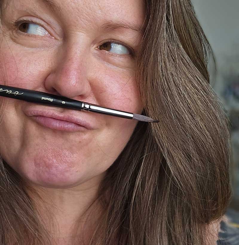 Artist Aliya Bodnar playfully holding a brush in her studio — capturing the joyful side of the creative process.