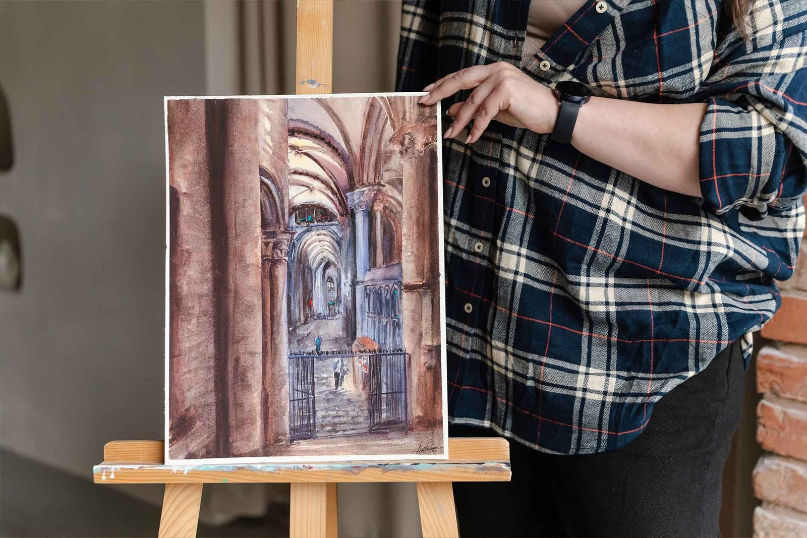 Aliya Bodnar holding a watercolour painting in her studio, preparing for an exhibition.