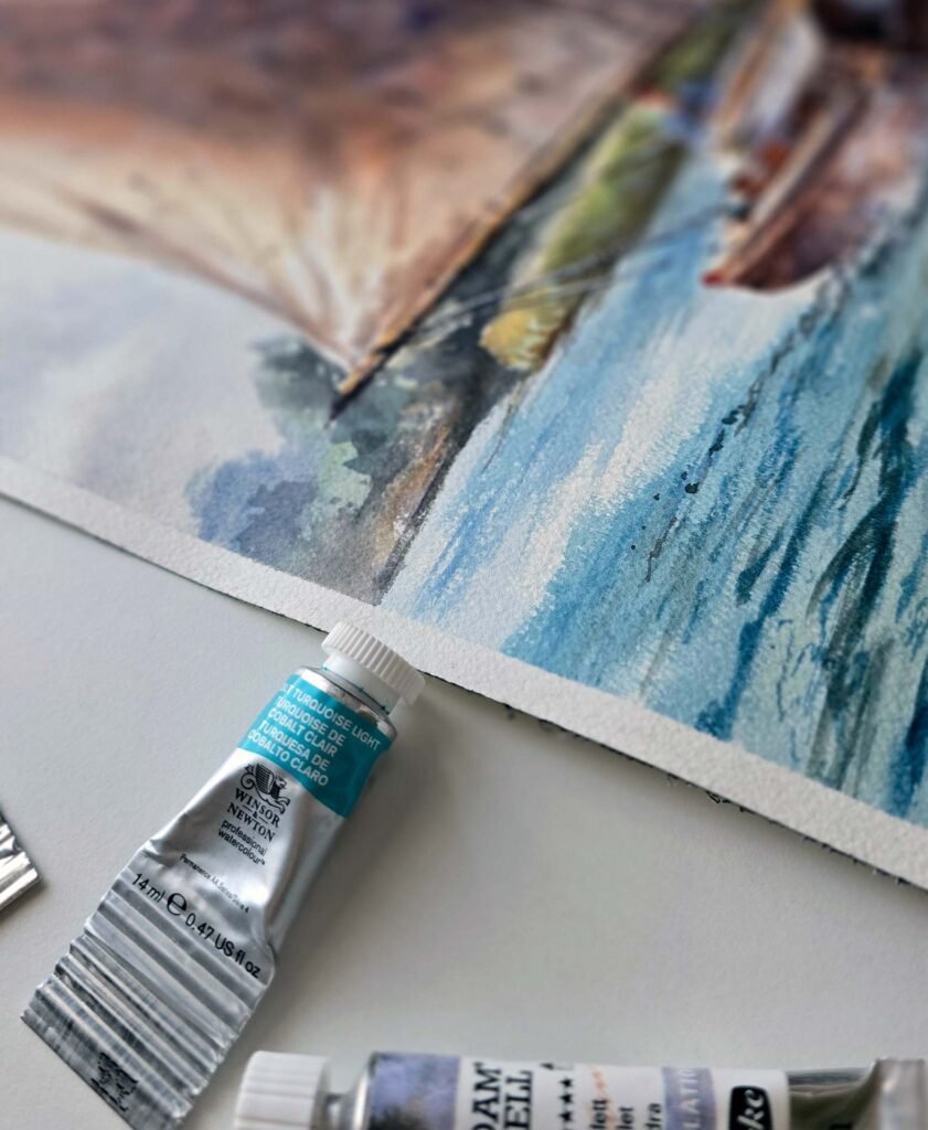 Close-up of Sailing Stillness, an original watercolour painting by Aliya Bodnar, showing blue water, part of the sailing boat and layered watercolour washes.